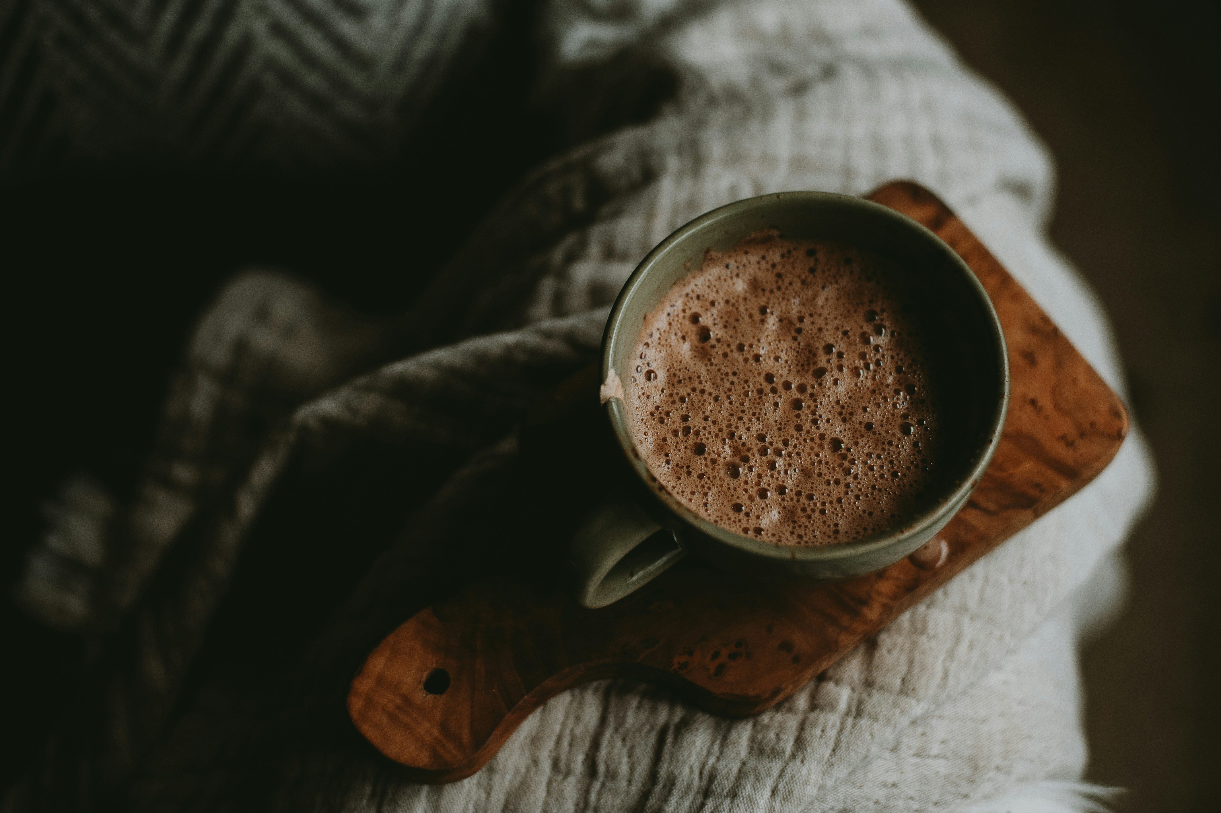 Tasse de chocolat chaud posée sur une planche en bois et un plaid douillet, évoquant l’ambiance cocooning de l’automne